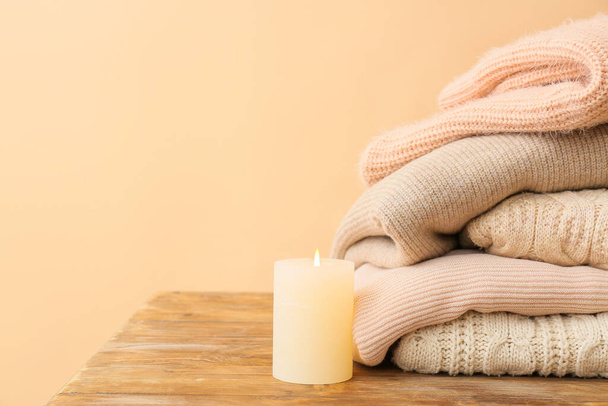 Stylové teplé oblečení se svíčkou na stole na barevném pozadí - Fotografie, Obrázek