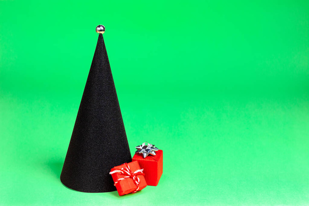 Black Christmas tree in the form of a cone in a modern style with a red gift on a green background - Fotó, kép