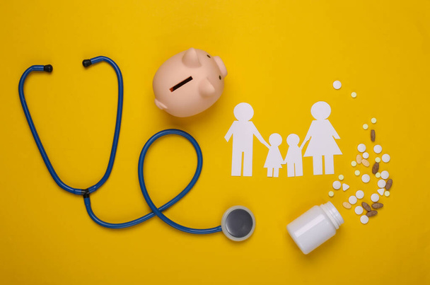 Stethoscope, paper chain family, piggy bank and pills on yellow background, health insurance concept - Photo, Image