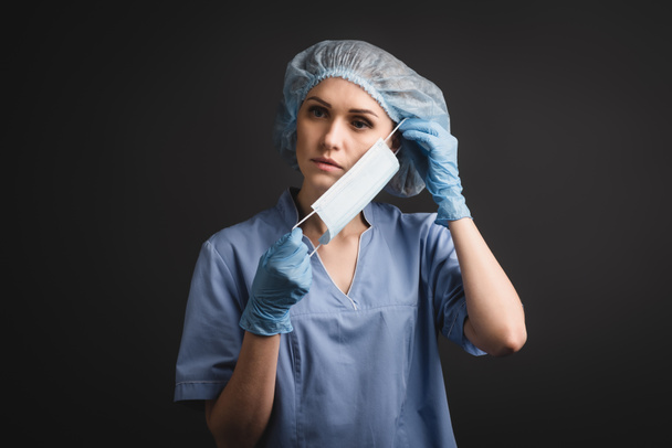 enfermera en gorra médica con máscara aislada en gris oscuro - Foto, Imagen