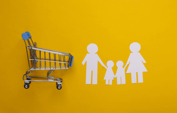 Papierfamilie zusammen und Supermarkt-Einkaufswagen auf gelbem Grund. Familieneinkauf. - Foto, Bild