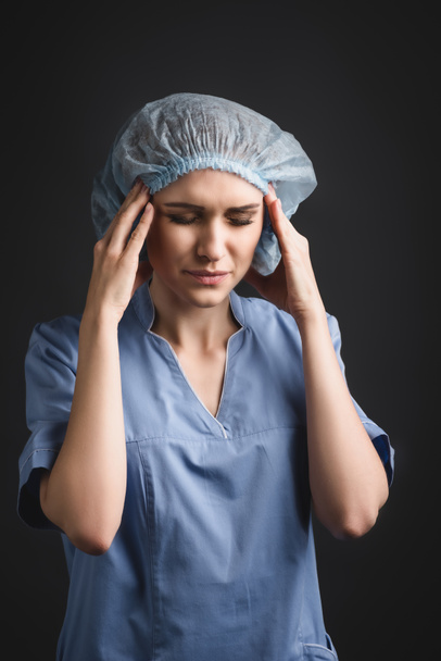 enfermera cansada con los ojos cerrados que sufren de migraña aislada en gris oscuro - Foto, Imagen