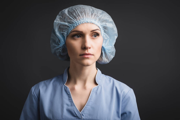 nurse in medical cap looking away isolated on dark grey - Fotó, kép