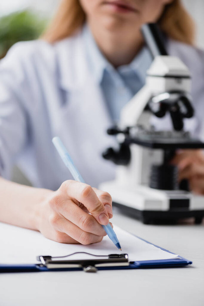 обрезанный вид ученого, пишущего на планшете возле микроскопа на размытом фоне - Фото, изображение