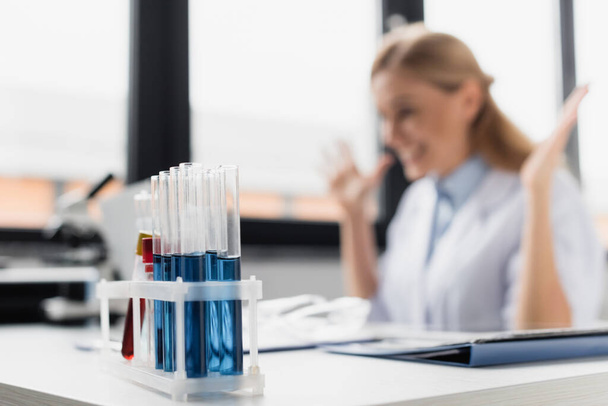 test tubes with samples near cheerful scientist on blurred background  - Foto, Bild