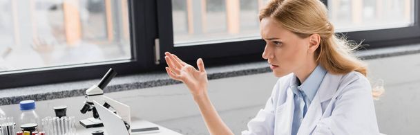 displeased scientist gesturing near microscope in lab, banner - Fotó, kép