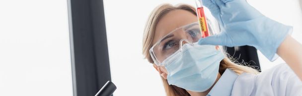 scientist in medical mask and goggles holding test tube with covid lettering, banner - Photo, Image