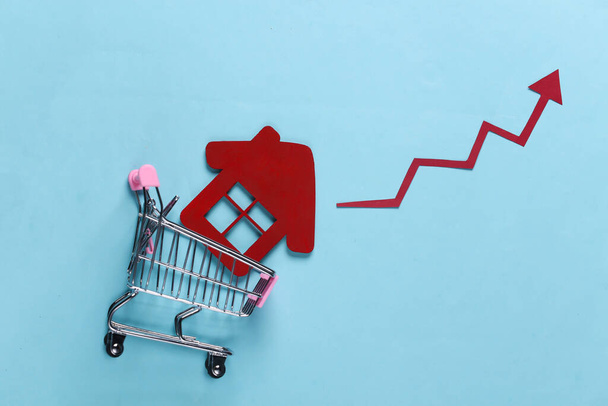 The concept of boosting house sales. Shopping trolley with home and growth arrow on a blue background. Top view - Photo, Image