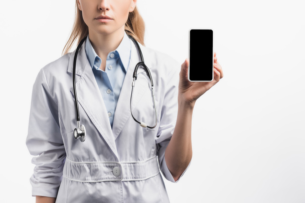 corte vista de enfermeira em casaco branco segurando smartphone com tela em branco isolado no branco - Foto, Imagem