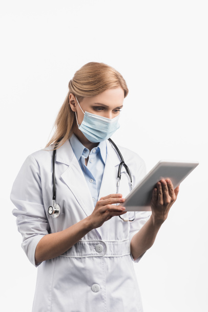 enfermera en máscara médica y bata blanca usando tableta digital aislada en blanco  - Foto, imagen