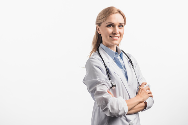 joyful nurse in white coat standing with crossed arms isolated on white - Фото, изображение