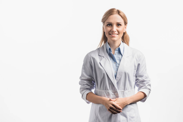 felice infermiera in cappotto bianco in piedi con le mani serrate isolate su bianco - Foto, immagini