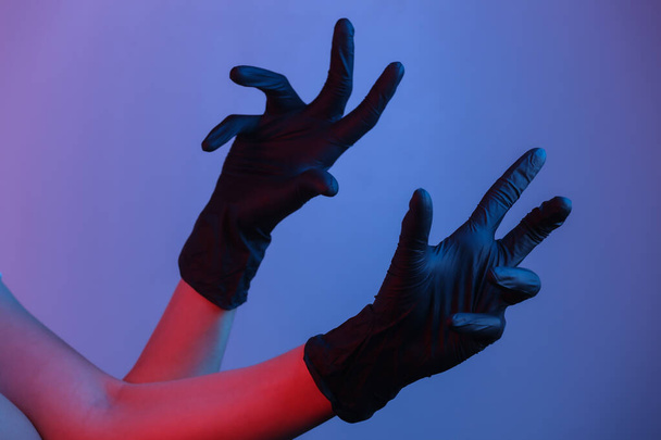 Mani femminili in guanti di lattice nero. Luce al neon gradiente - Foto, immagini