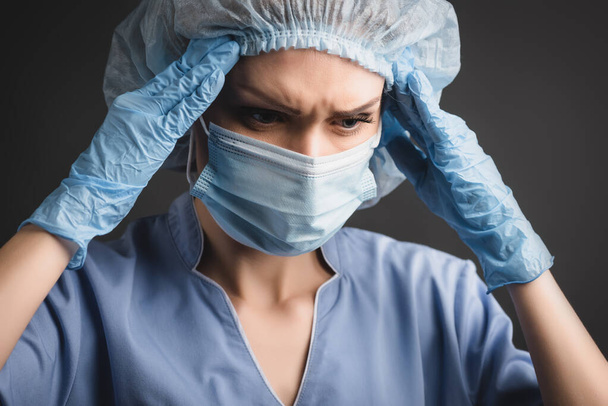 infermiere in berretto e maschera medica affetto da emicrania isolato su grigio scuro - Foto, immagini