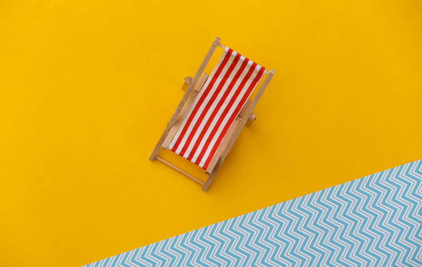Striped mini beach deck chair on yellow blue background. Symbol of beach holidays, resort.  Relax, Summer minimal concept - Fotó, kép