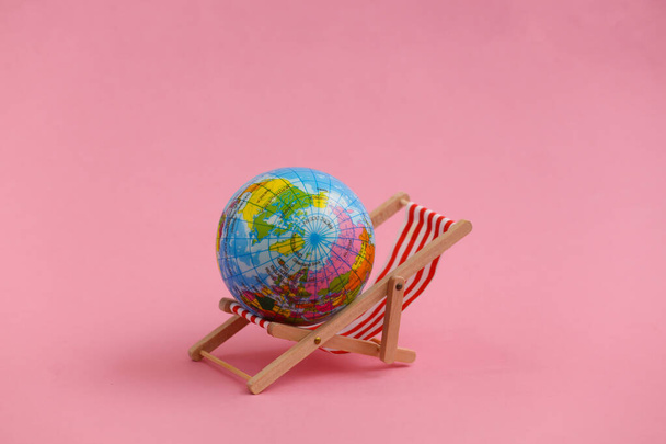 Mini-Strandkorb mit Globus auf rosa Hintergrund. Symbol des Strandurlaubs, Ferienort. Entspannen, Sommer, Minimalkonzept. - Foto, Bild