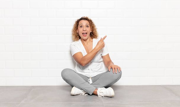 middle age woman looking excited and surprised pointing to the side and upwards to copy space - Foto, imagen