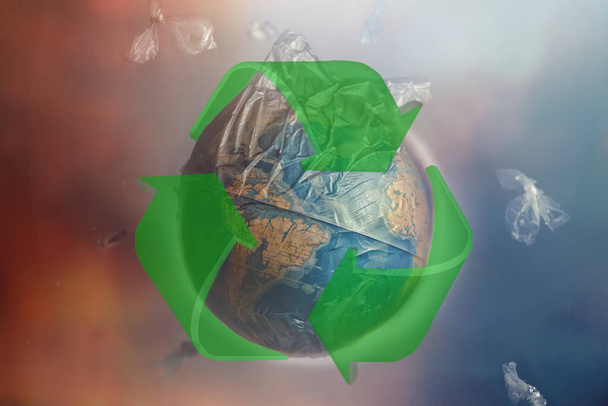Глобус планеты Земля в мусорном мешке. Зеленый знак утилизации. Концепция сохранения окружающей среды и ее ресурсов, переработки сырья. Красный и синий оттенки. - Фото, изображение