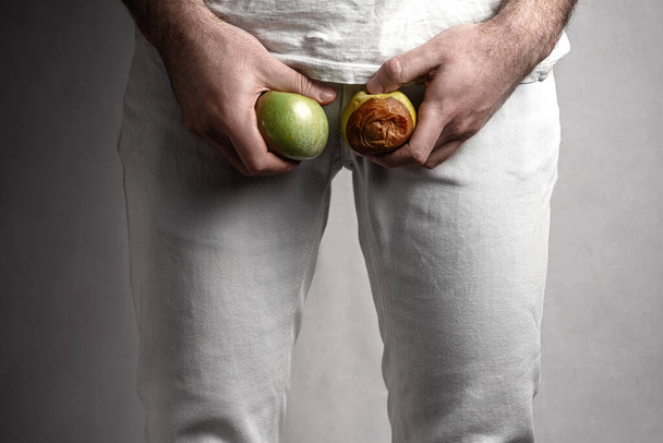A man at the level of the genitals , holding a ripe and rotten apple. Male suffering with pain in the urogenital system. Disease for men. The concept of protection of sexually transmitted infections. Close up. - Photo, Image