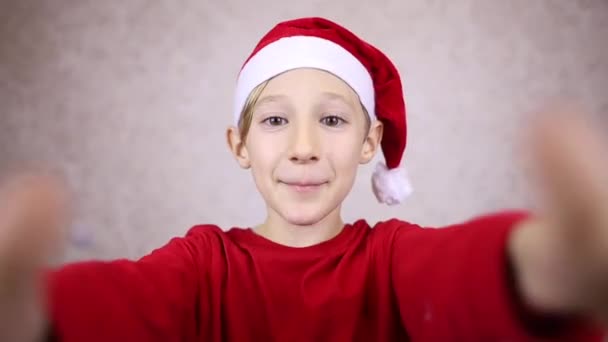a boy in a red Santa hat wishes a happy new year and Christmas - Кадры, видео