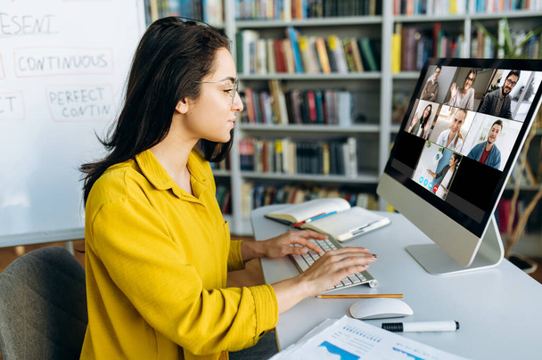 Online oktatás. Egy diáklány online tanul otthon, egy számítógép monitorra koncentrál, amire egy csoport másik diák és egy tanár információt mond. - Fotó, kép