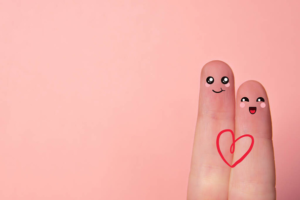 Пальцы любви. Крупный план двух пальцев на розовом фоне с нарисованными улыбающимися лицами. Понятие любви и Валентина. Копировальное пространство - Фото, изображение