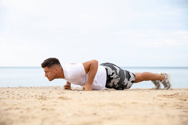 Muscular man doing push up on beach. Body training - Valokuva, kuva