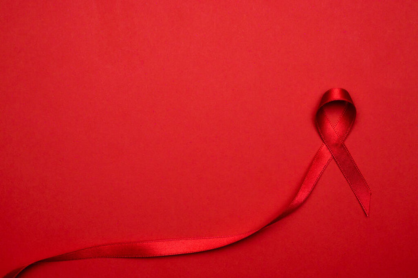 Szia, kisegítő. Piros szalag szimbólum HIV világnap sötét vörös háttér. Tudatosság segédeszközök és rák. Az öregedés egészségügyi hónapjának koncepciója - Fotó, kép