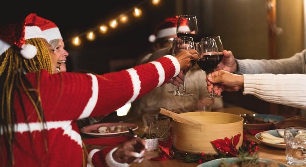 Happy multiracial senior friends toasting with red wine glasses during Christmas holidays dinner celebration on patio house party - Photo, Image