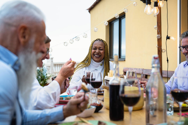 Amigos seniores multirraciais felizes se divertindo jantando juntos no pátio da casa Pessoas idosas estilo de vida e conceito de comida - Foto, Imagem