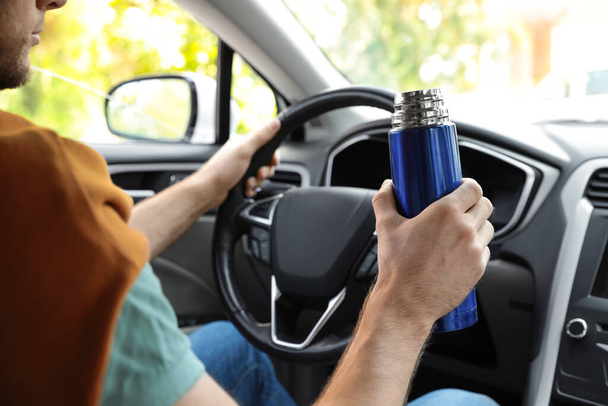 Man with thermos driving car, closeup view - Foto, imagen