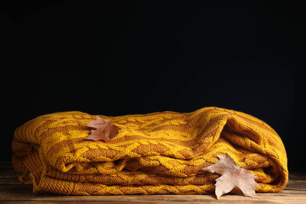 Orange knitted plaid with dry leaves on wooden table. Space for text - Photo, image