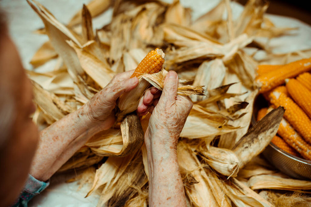 Imagen de una anciana pelando y seleccionando con las manos maíz en una mesa. - Foto, imagen