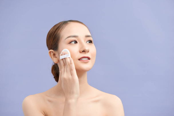 Beautiful woman applying dry powder using cosmetic cushion on her facial skin. Photo of attractive girl with perfect makeup on beige background. Beauty concept - Fotó, kép