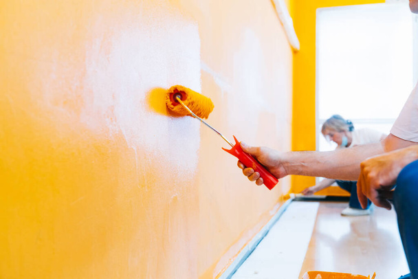 Painting an orange wall with a roller and brush. Man and woman doing reforms in the room, house or local business. Painter staff. - Foto, Imagen