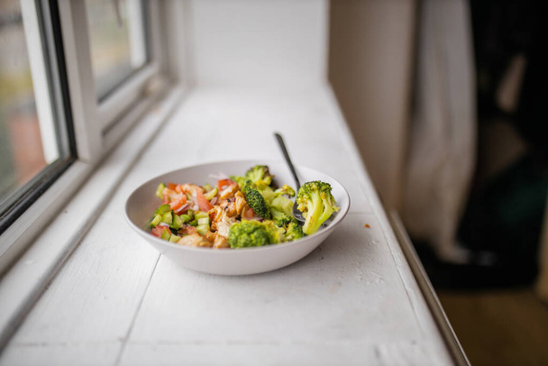 Брокколи и куриный салат на белой миске рядом с окном - Фото, изображение