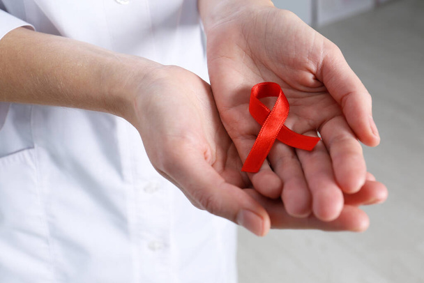 Лікар тримає червону стрічку в приміщенні, крупним планом. Всесвітній день хвороби СНІДу
 - Фото, зображення