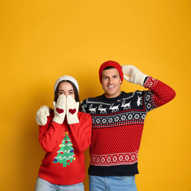 Couple in Christmas sweaters, knitted mittens and hats on yellow background - Foto, imagen