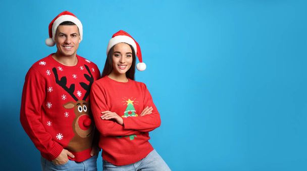 Couple in Christmas sweaters and Santa hats on blue background, space for text - 写真・画像
