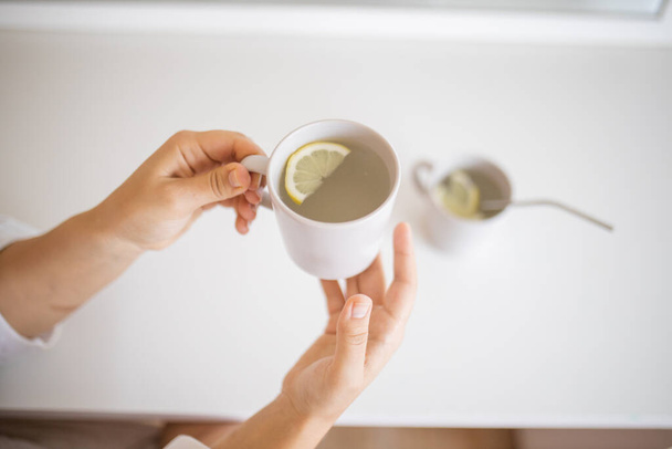 Kezek kezében egy csésze citromos tea citromszelettel - Fotó, kép