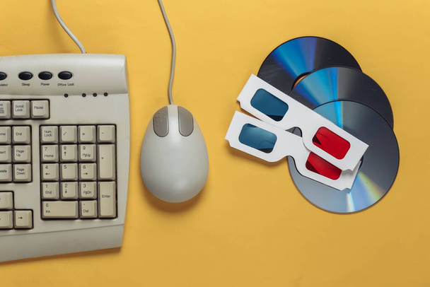 Retro entertainment. Old-fashioned keyboard, pc mouse, compact discs, anaglyph stereo glasses on a yellow background. Top view. Flat lay - Photo, Image