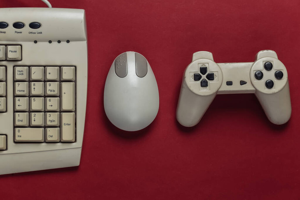 Retro entertainment. Ouderwetse pc muis, toetsenbord, gamepad op rode achtergrond. Bovenaanzicht. Vlakke plaat - Foto, afbeelding