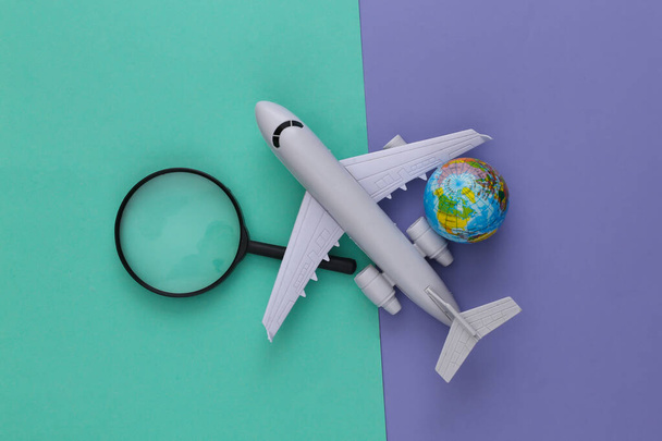 Reisconcept. Vliegtuig, vergrootglas met een globe op paarse blauwe achtergrond. Bovenaanzicht. Vlakke plaat - Foto, afbeelding