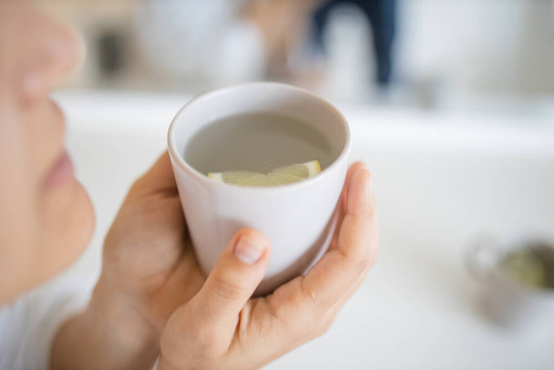 Woman gently blowing on a cup of lemon tea with a lemon slice inside - Foto, Imagen