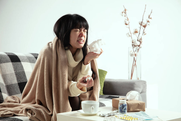 Woman wrapped in a plaid looks sick, ill, sneezing and coughing sitting at home indoors - Photo, Image