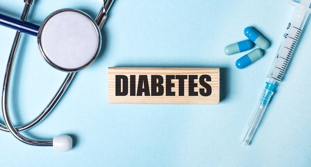На синем фоне стетоскоп, шприц и таблетки и деревянный блок со словом "диабет". Медицинская концепция - Фото, изображение