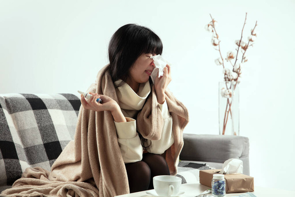 Woman wrapped in a plaid looks sick, ill, sneezing and coughing sitting at home indoors - Fotoğraf, Görsel