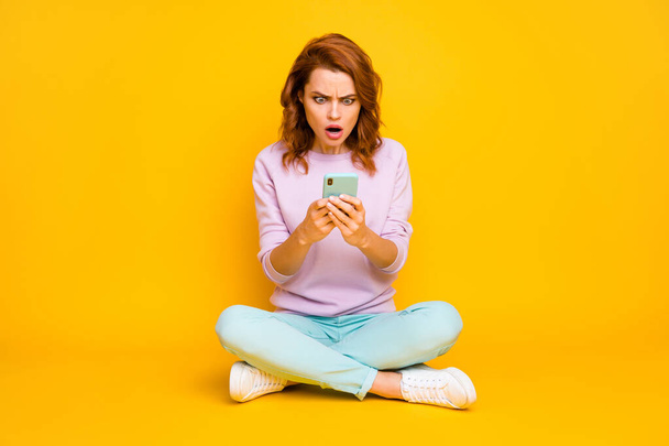 Full body photo shocked astonished woman sit legs crossed use smartphone read horrible social media news impressed scream wear teal pink shoes jumper isolated yellow color background - Foto, Imagen