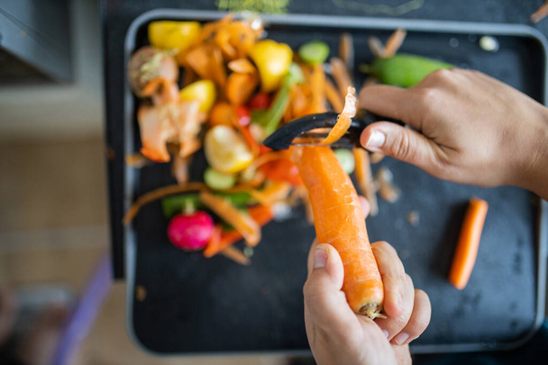 Le mani femminili che sbucciano una carota sopra spazzatura organica - Foto, immagini