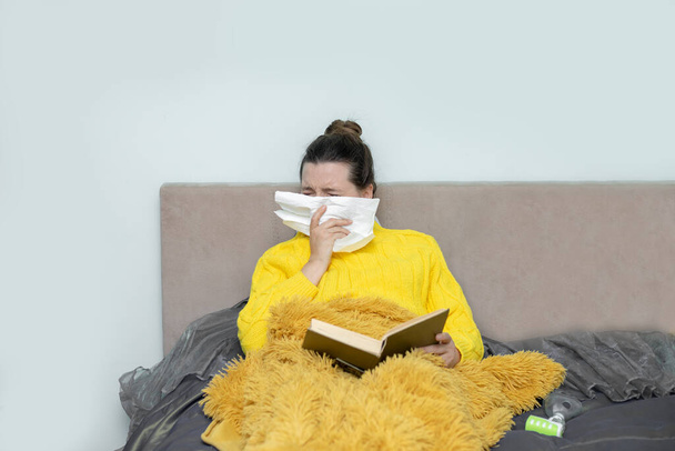 Frau liest Buch im Bett, mit Papierserviette niest, bekommt Allergiesymptome, erkältet sich, bleibt zur Selbstquarantäne isoliert. Konzept Hausquarantäne, Prävention COVID-19, Coronavirus. Foto - Foto, Bild